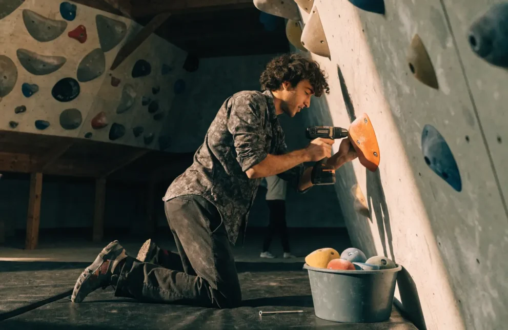 Routenbauer schraubt einen neuen orangen Griff an die Boulderwand